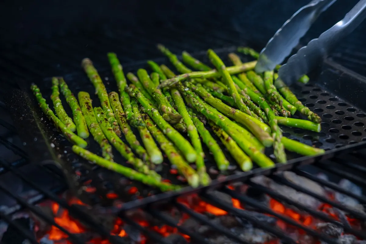 Grüner Spargel wird mit Olivenöl und Gewürzen auf einem Grill im Freien zubereitet.