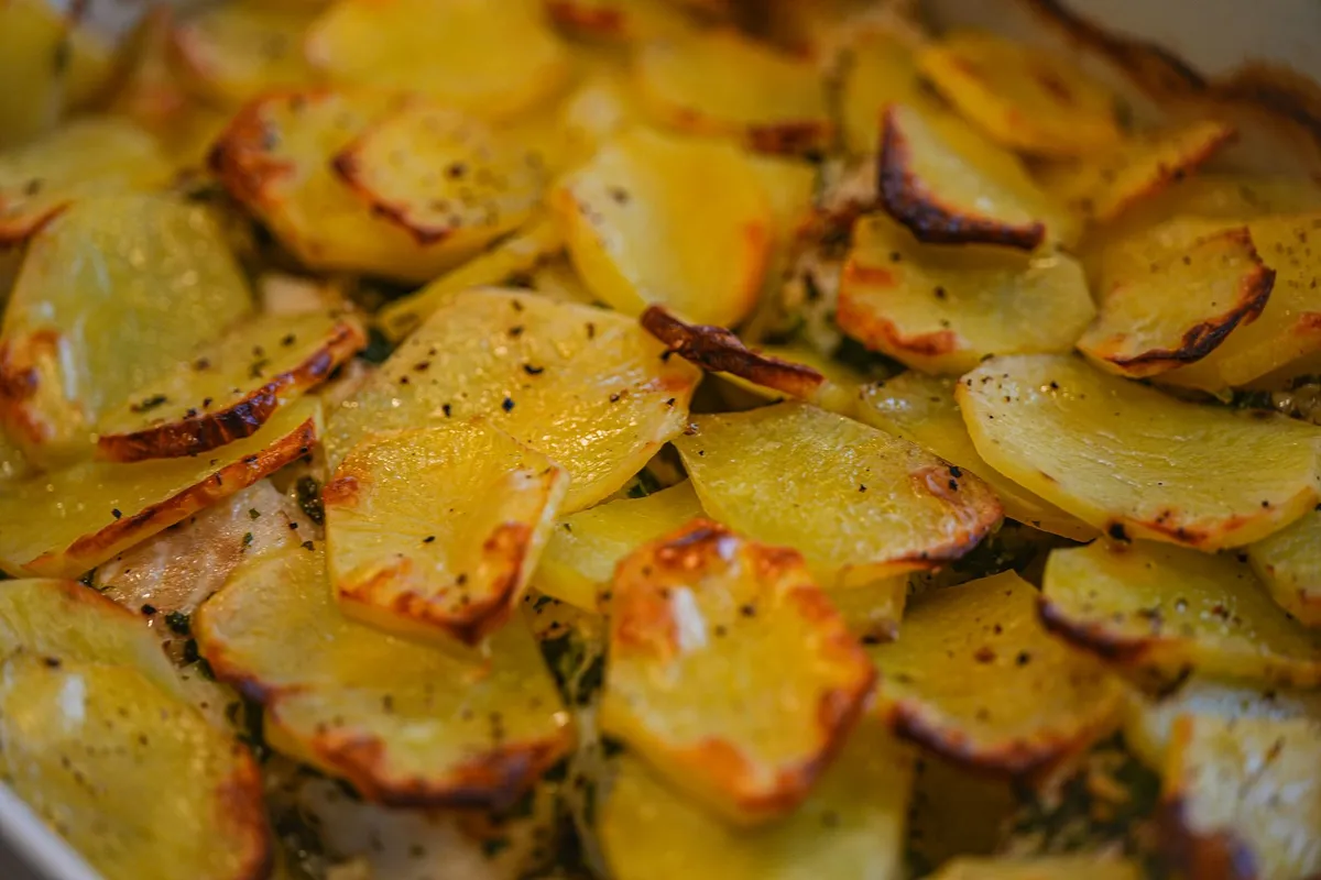 Dünn geschnittene rohe Kartoffelscheiben mit frischen Kräutern auf einem Holzbrett.