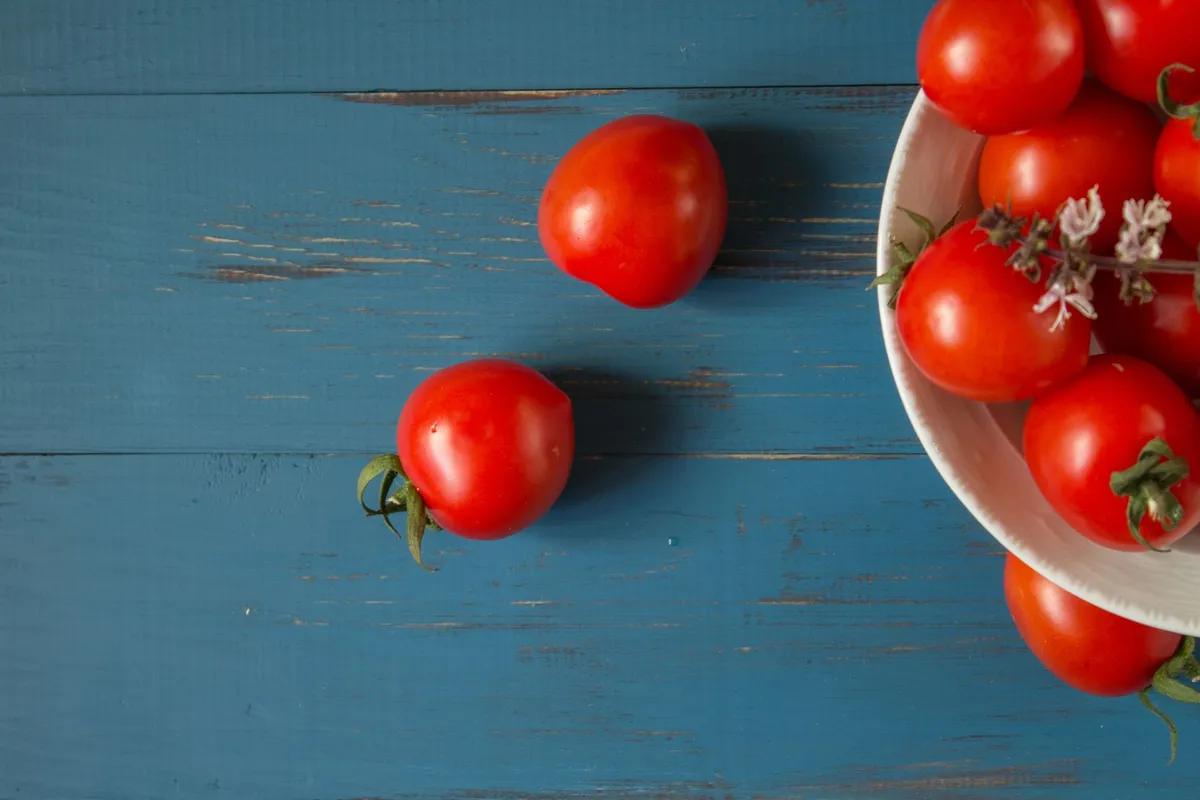 Ein angerichteter Tomatensalat mit Basilikum in einer Schale auf einem Gartentisch.
